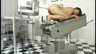 Brunette naked on the doc table with legs spread wide is prepared for toy penetrations
